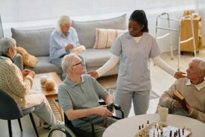 An older adult sitting comfortably and chatting via video call on a tablet with a caregiver nearby.