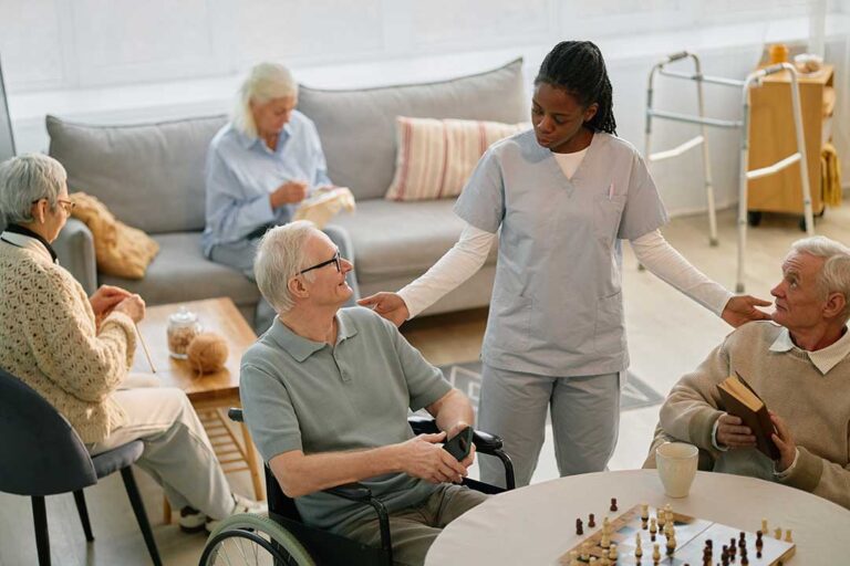 An older adult sitting comfortably and chatting via video call on a tablet with a caregiver nearby.
