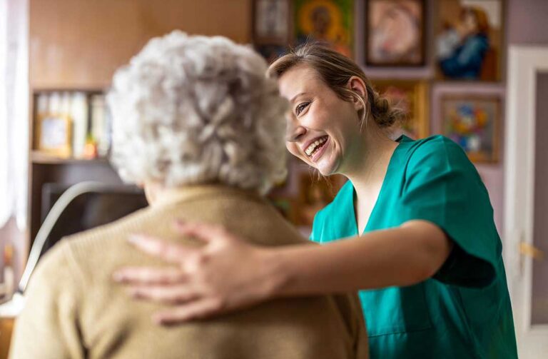 Family member and older adult talking quietly in a bright assisted living sitting room.