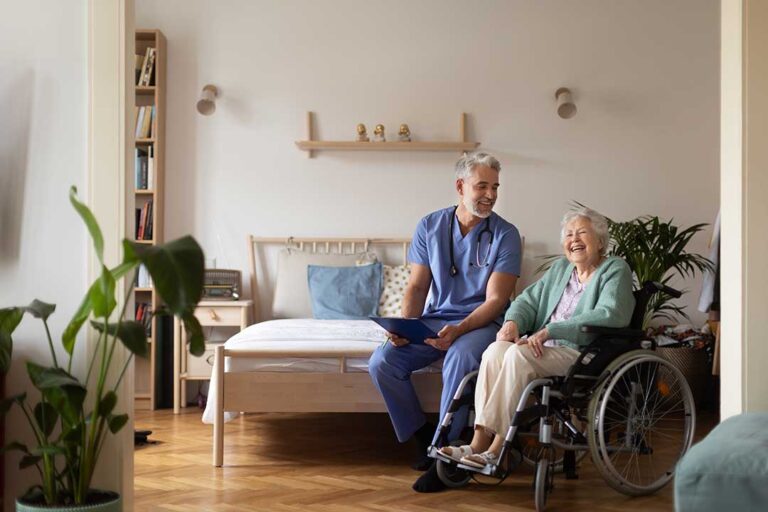 Nurse reviews a resident’s medication chart beside a senior in a bright assisted living room.
